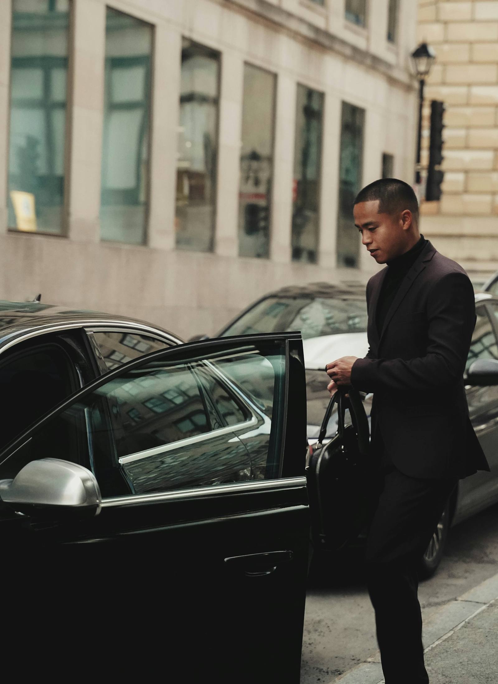 Chauffeur en costume sombre ouvrant la portière d'une berline noire